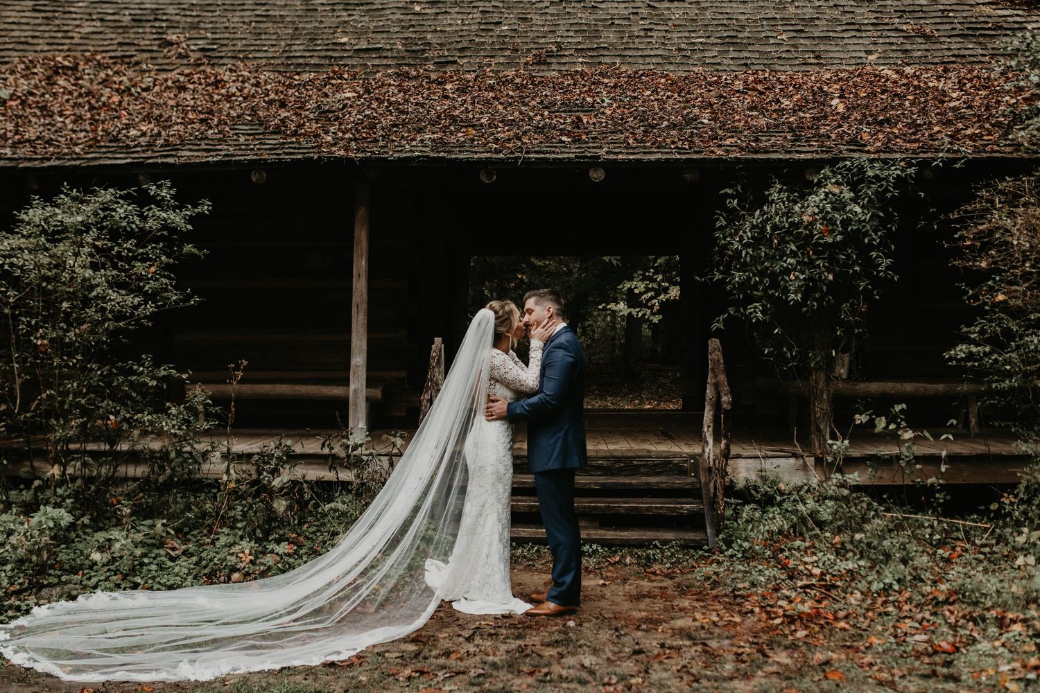 Rustic autumn wedding photography with fallen leaves and wooden architecture.