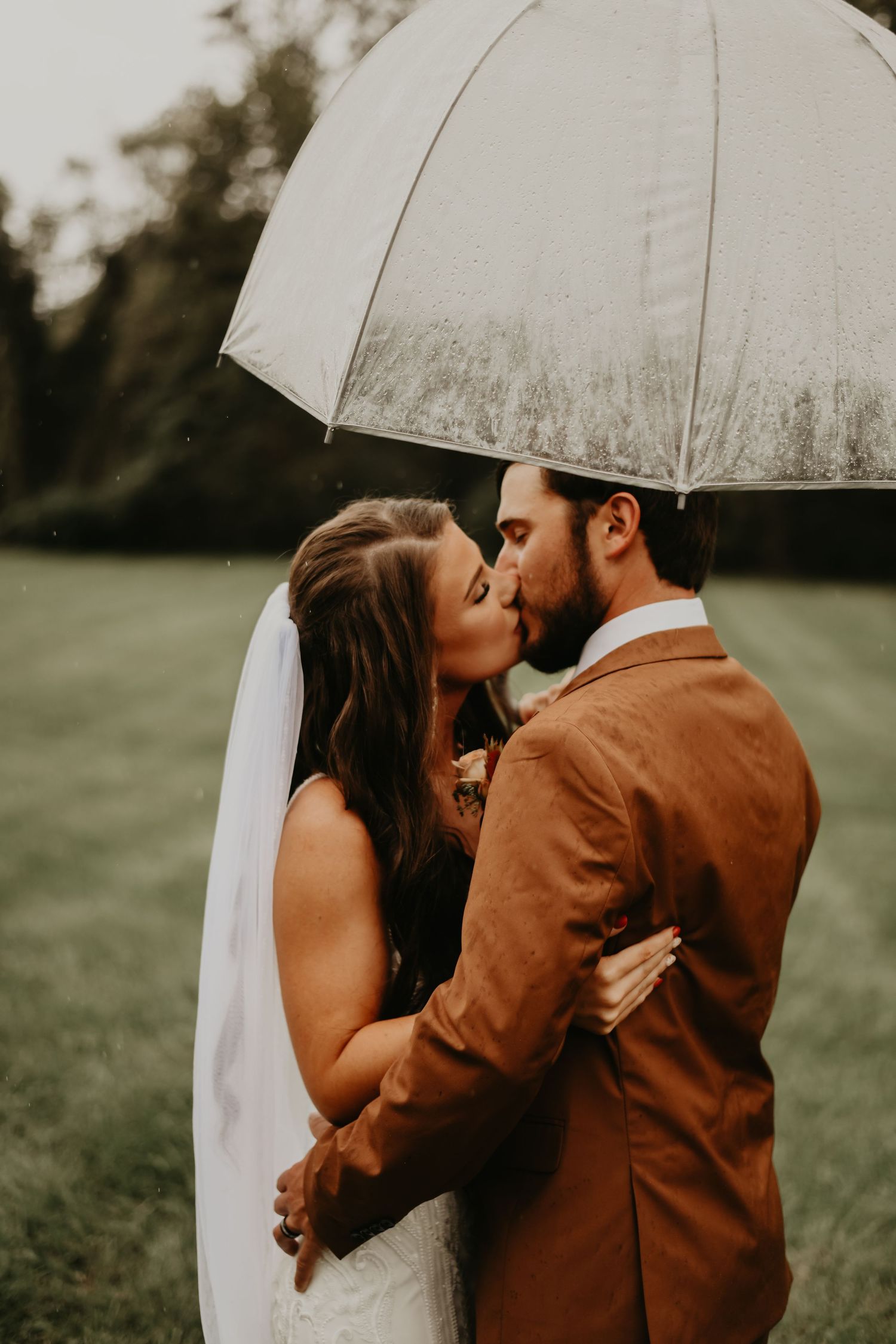 A romantic wedding moment captured under a white umbrella in a lush green field in Asheville North Carolina.