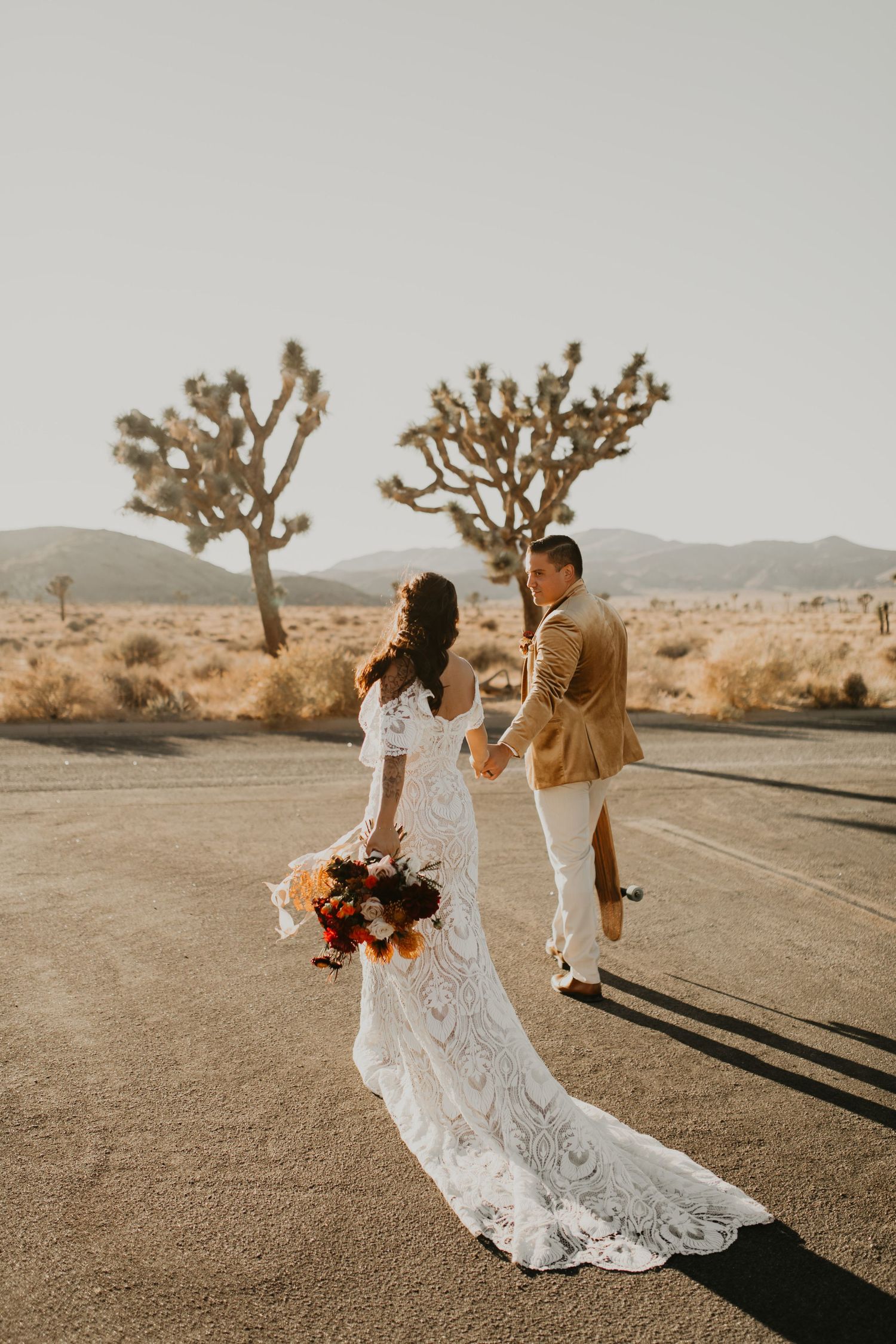 Bride and groom dancing on desert road surrounded by Joshua trees at sunset in California.