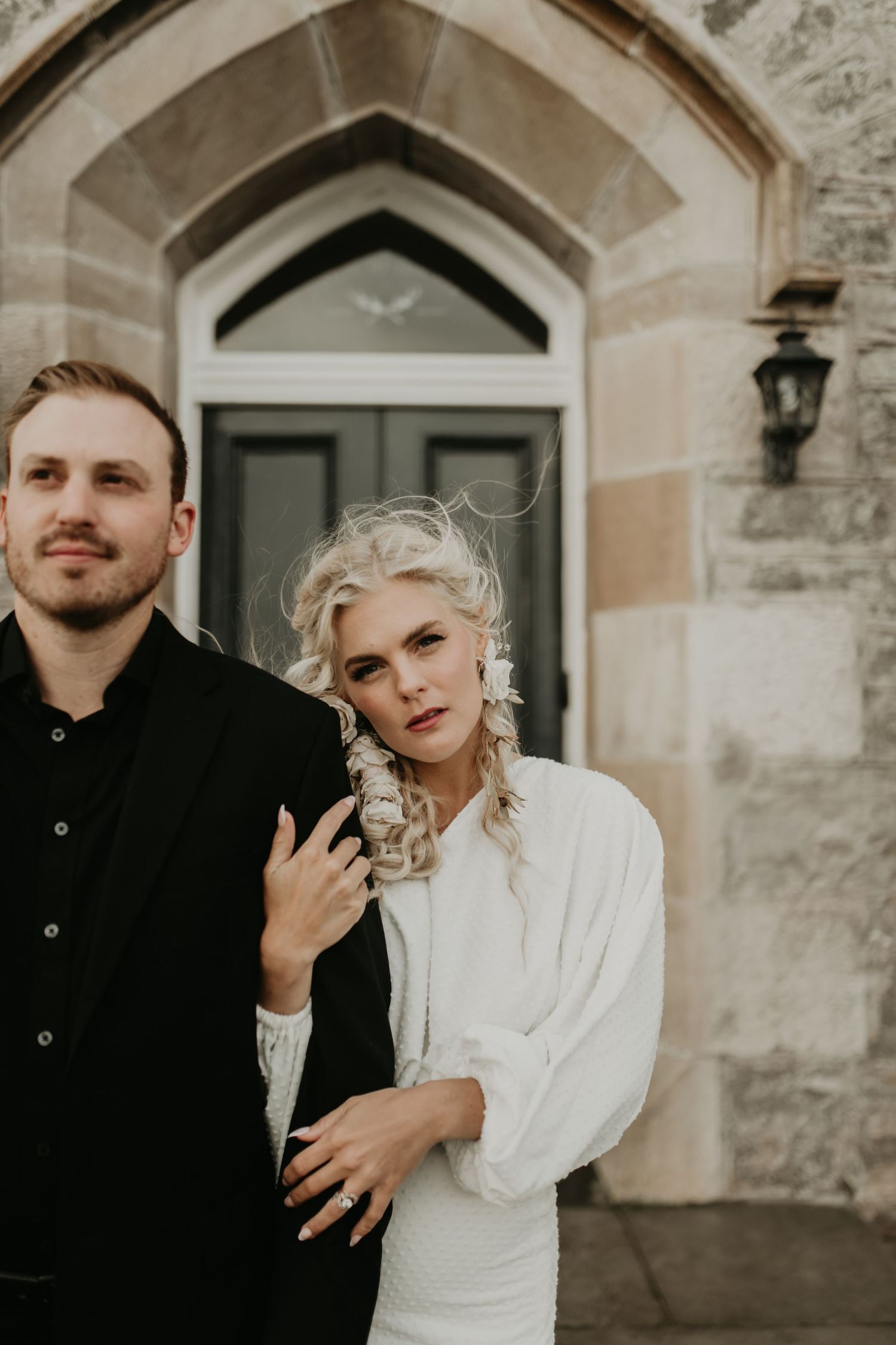 A couple poses against a stone building entrance wearing black and white formal attire in isle of skye Scotland.