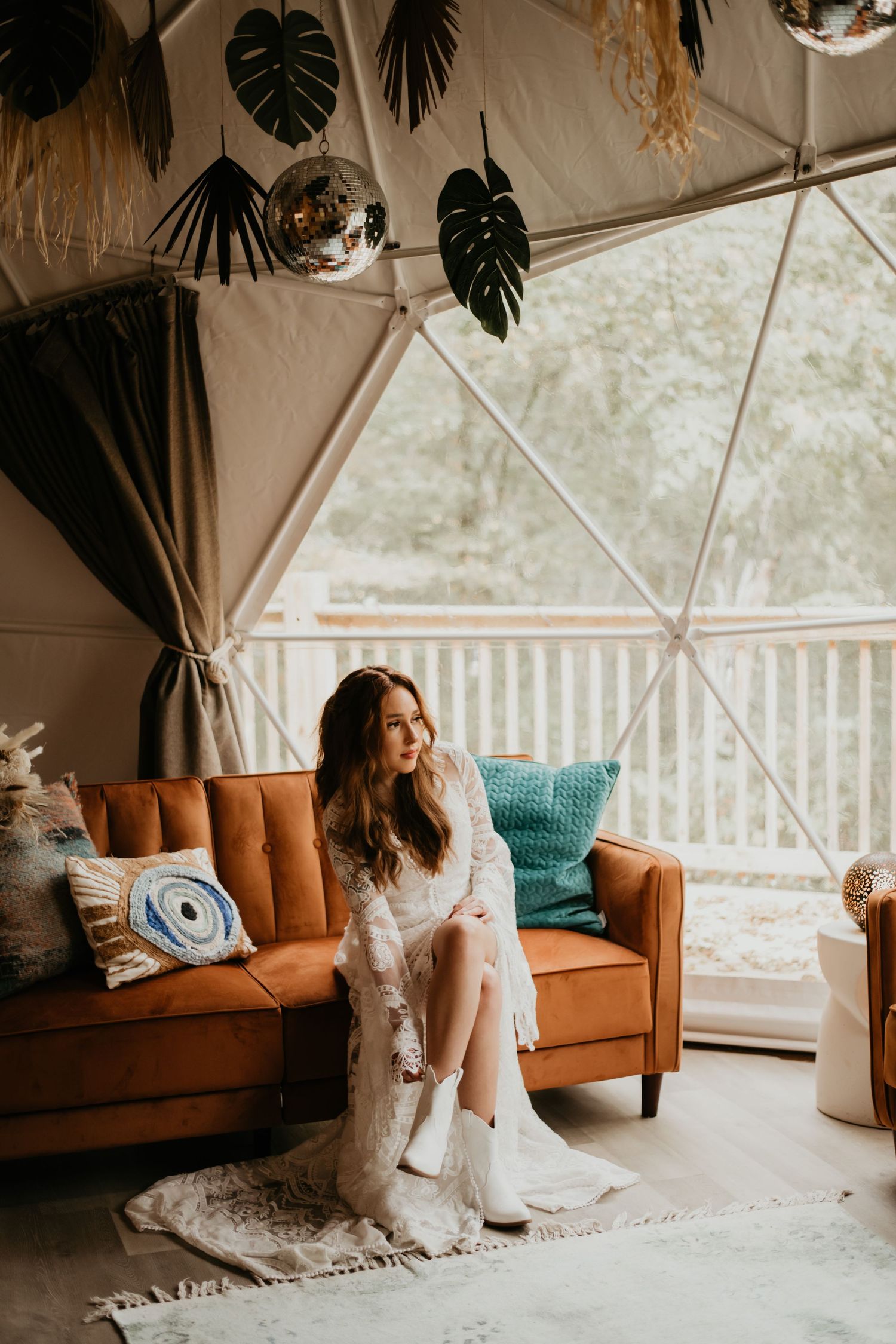 Wedding lounge setup with bohemian decor and orange velvet sofa in light-filled tent.