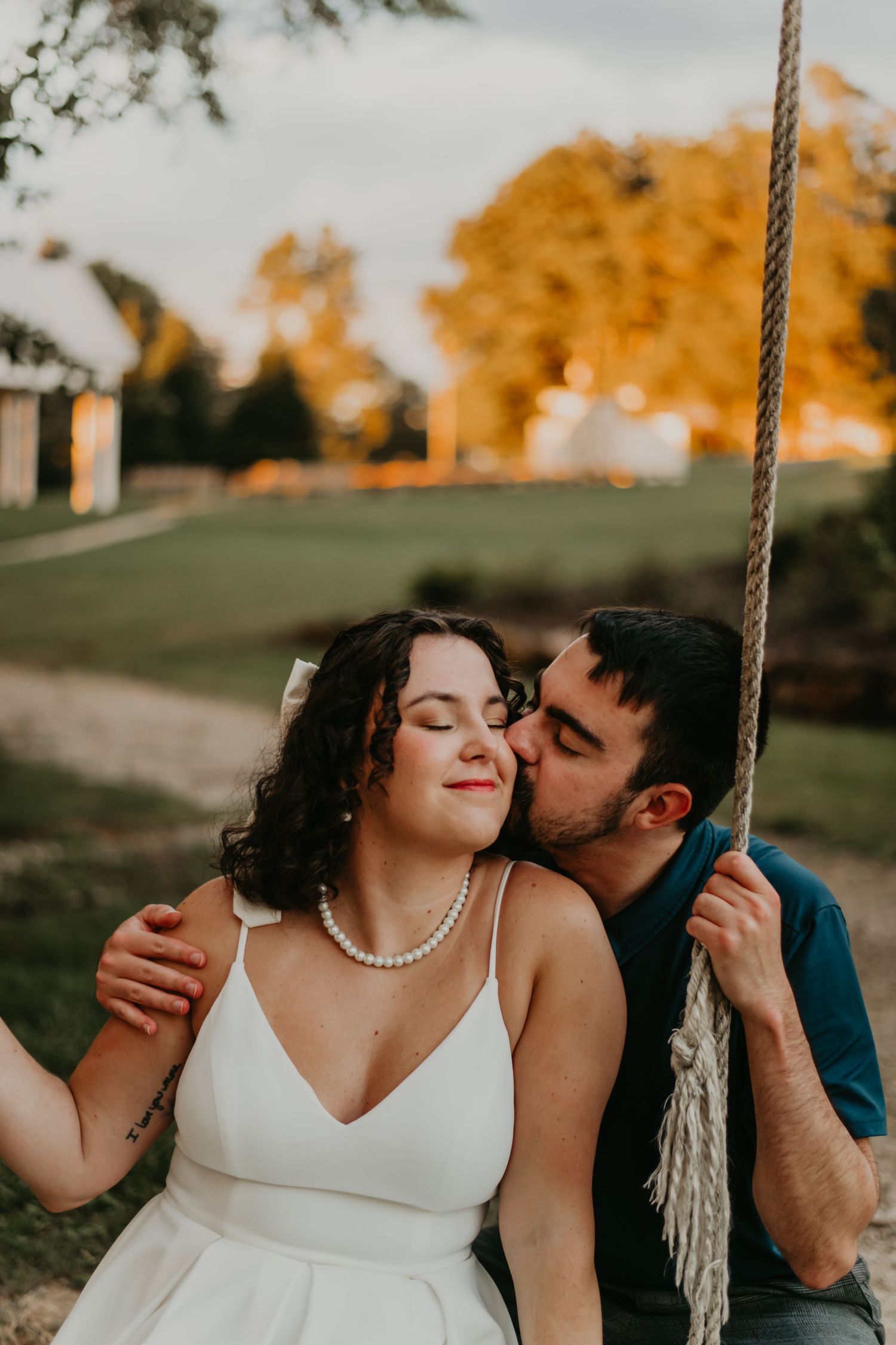 A romantic couple shares an intimate moment on a rope swing at sunset with autumn trees glowing golden in the background.