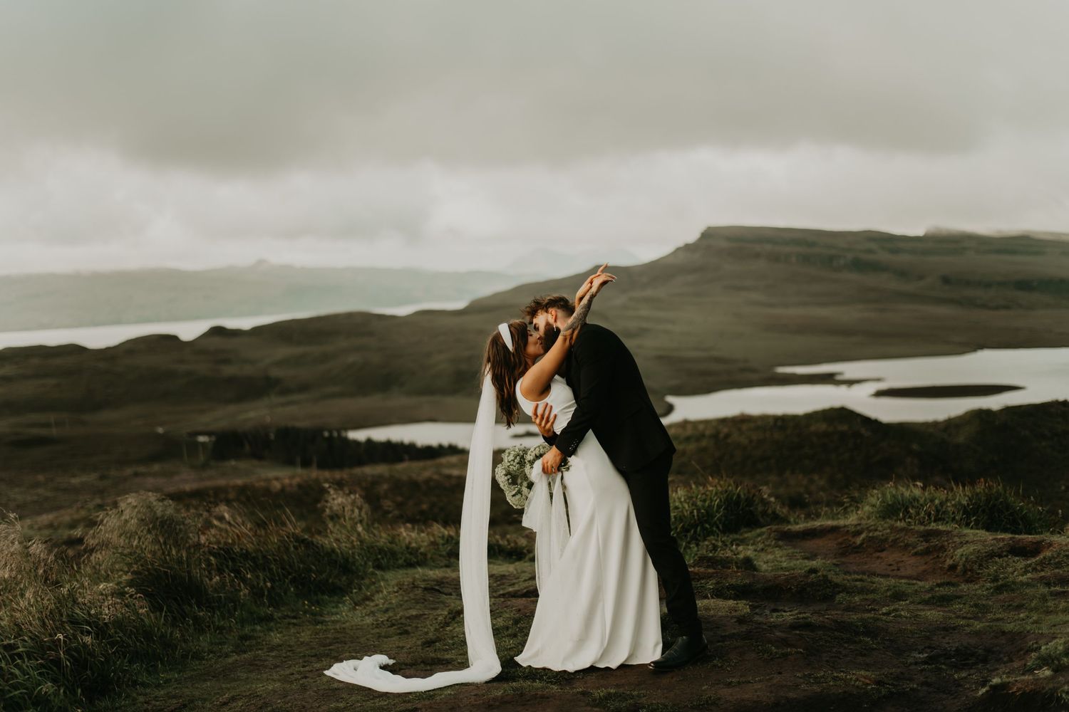 A couple embraces on a hilltop overlooking scenic Scottish lakes and rolling hills in isle of Skye Scotland.