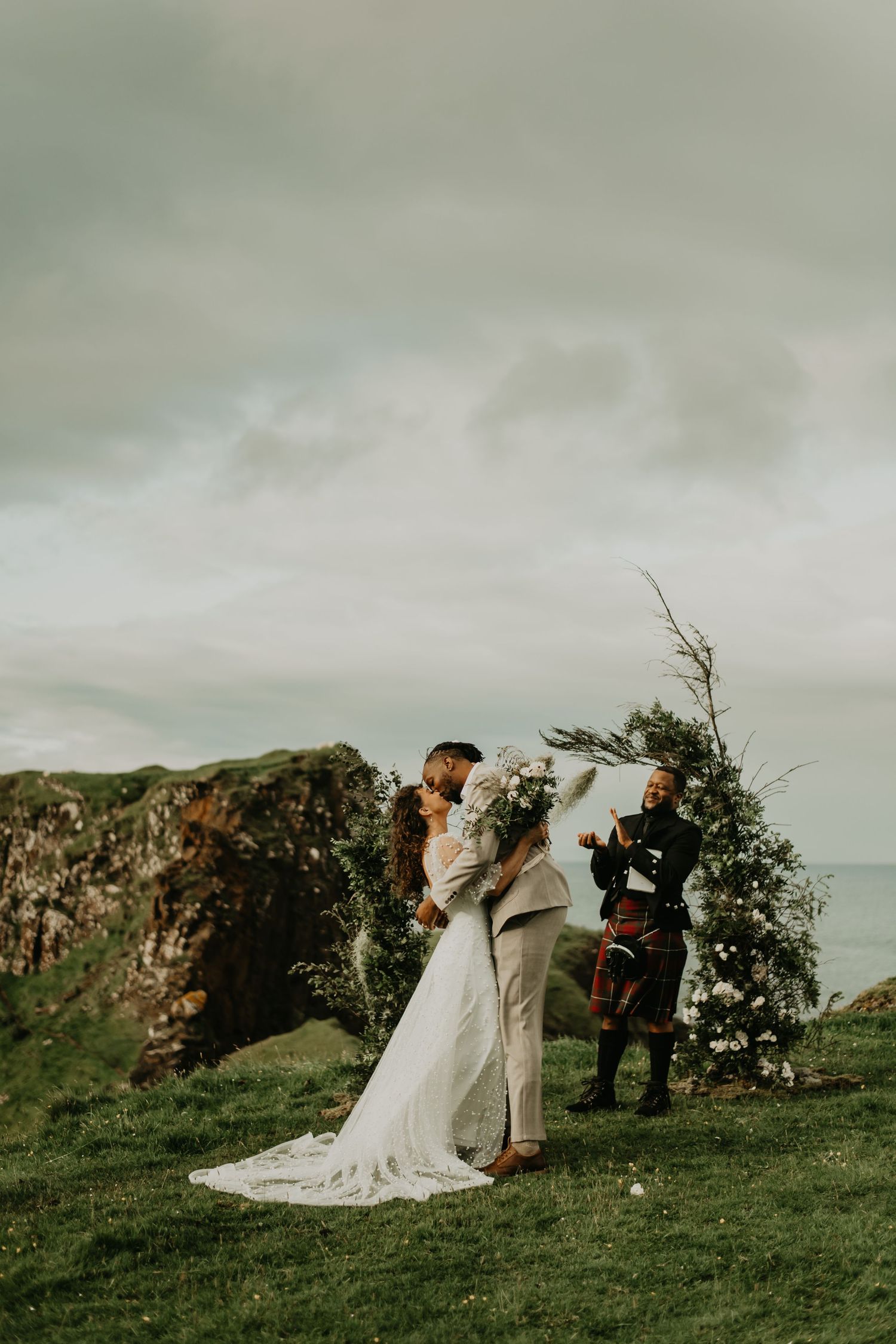 Wedding ceremony with bagpiper on scenic Scottish cliff overlooking the ocean in Isle of Skye Scotland.