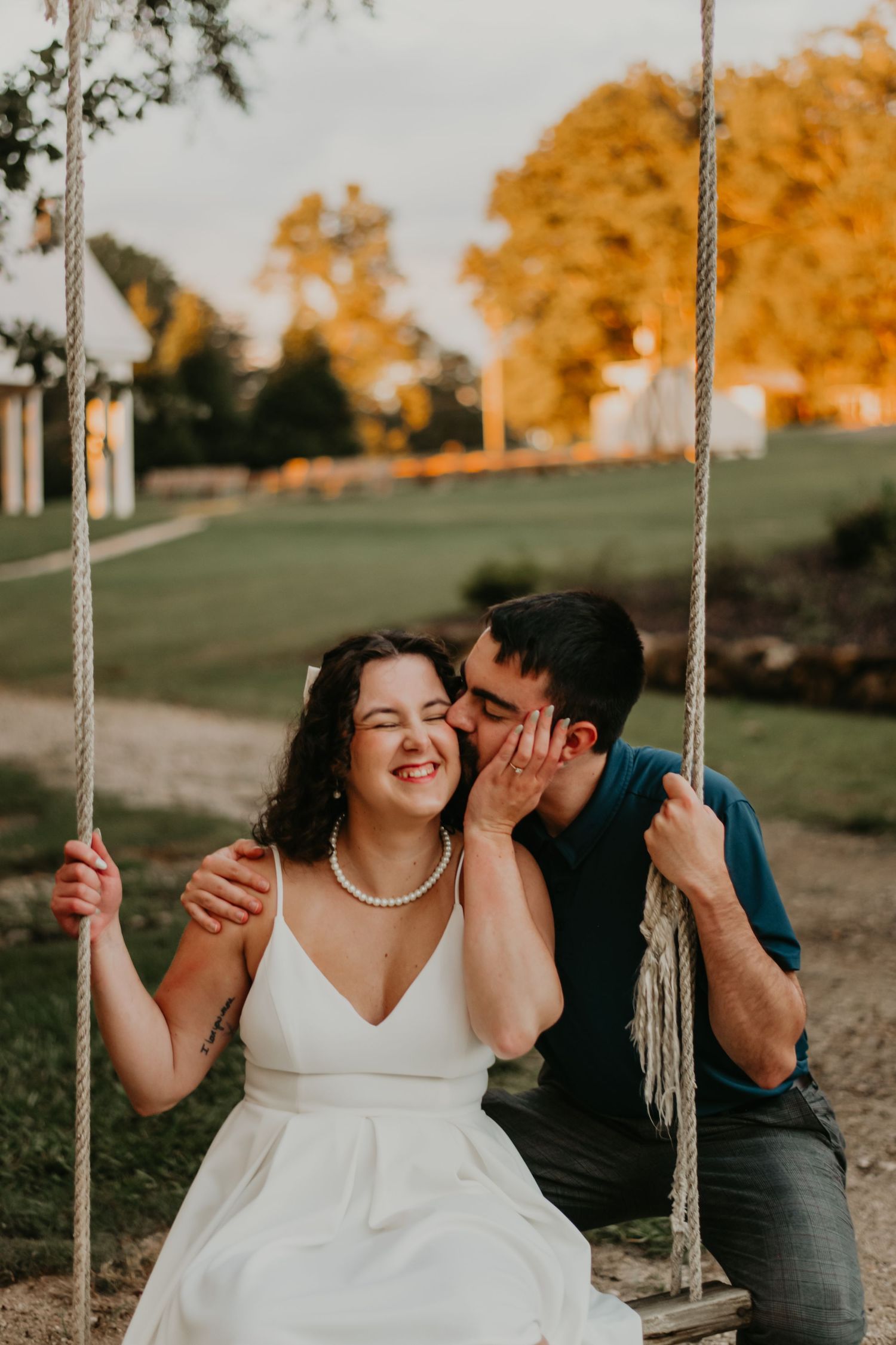 A romantic couple shares a joyful moment together on a rustic rope swing during sunset in an outdoor setting.