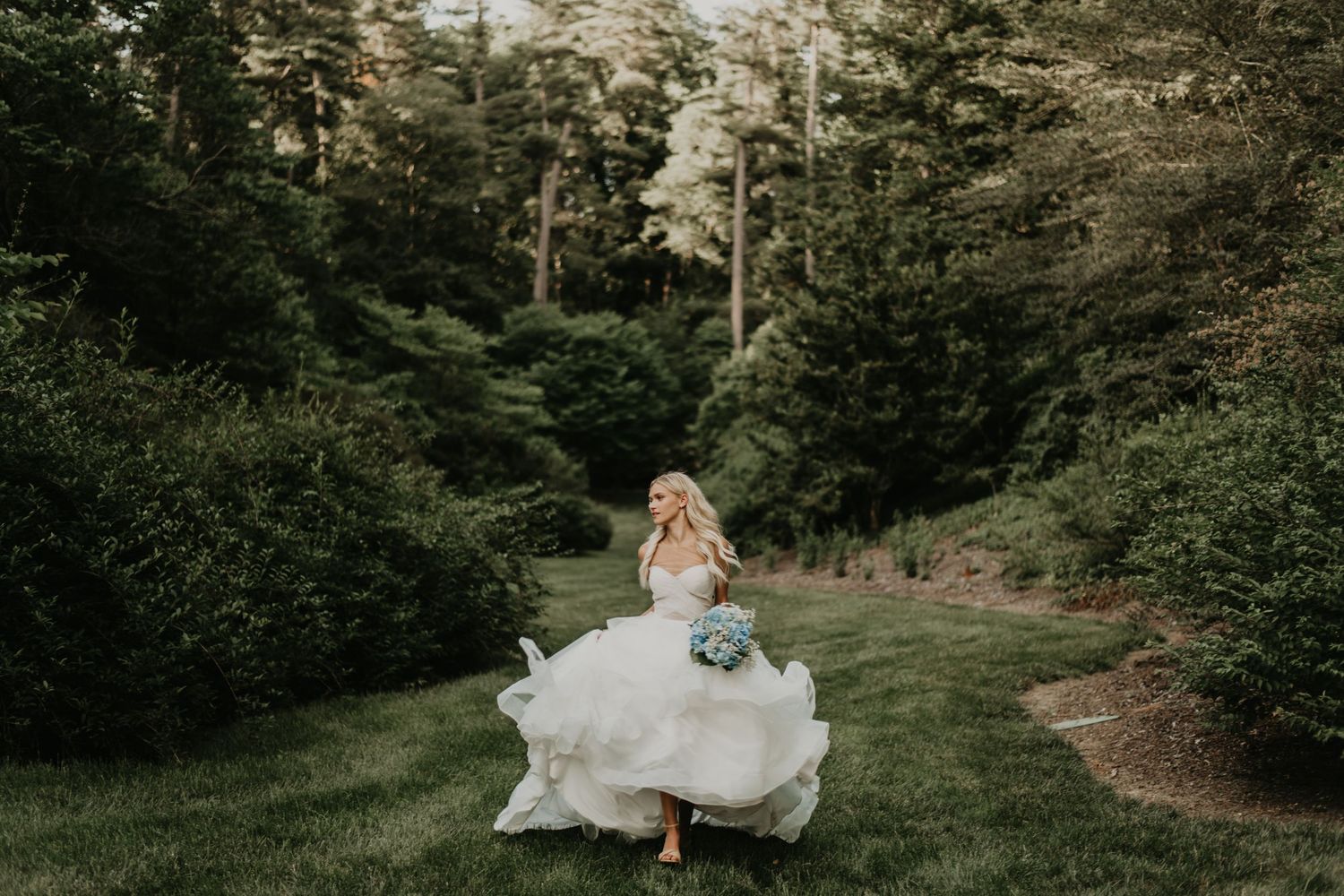 A flowing white wedding dress twirls through a lush forest path.