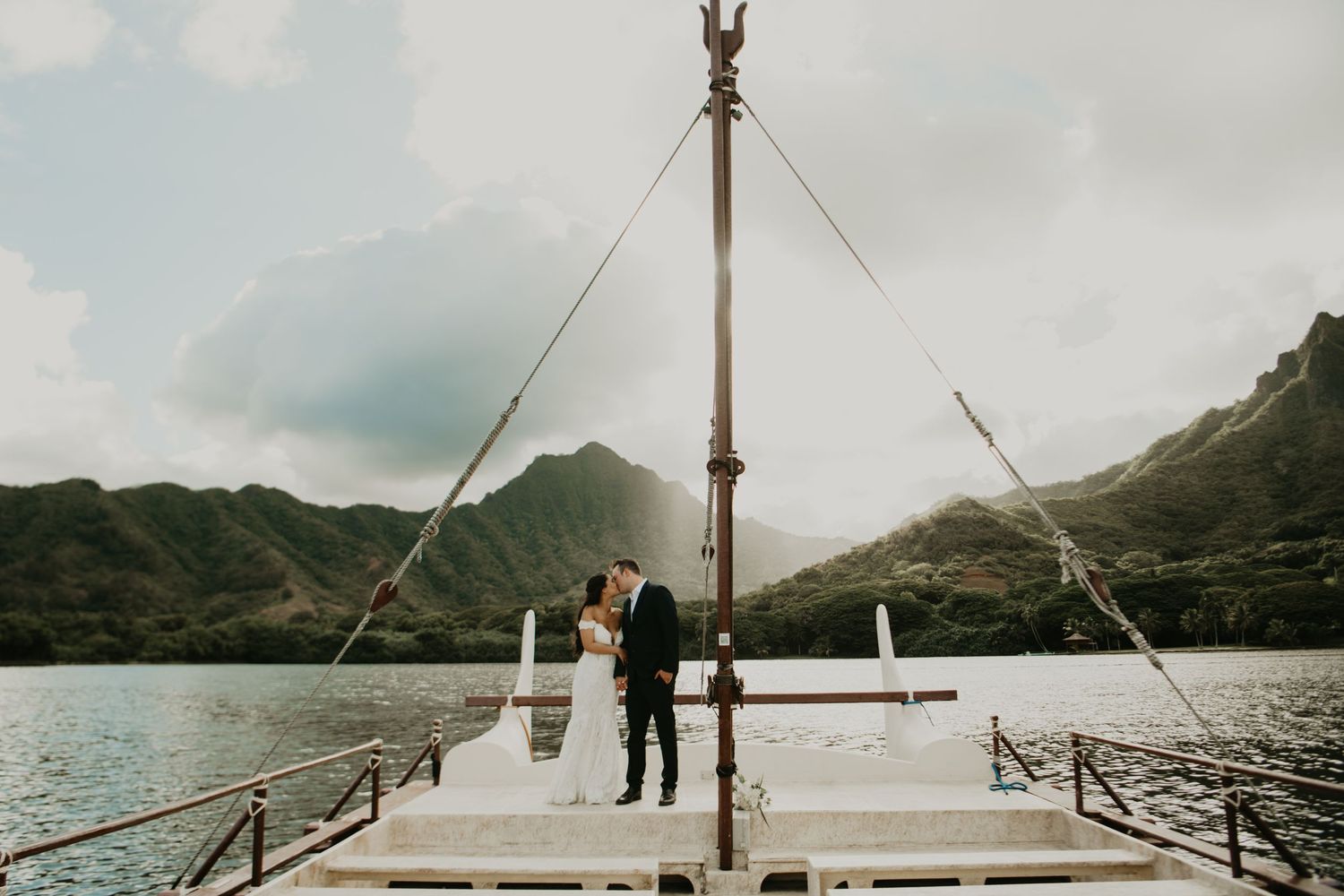 Wedding celebration aboard a boat with mountainous backdrop on a scenic lake in Hawaii.