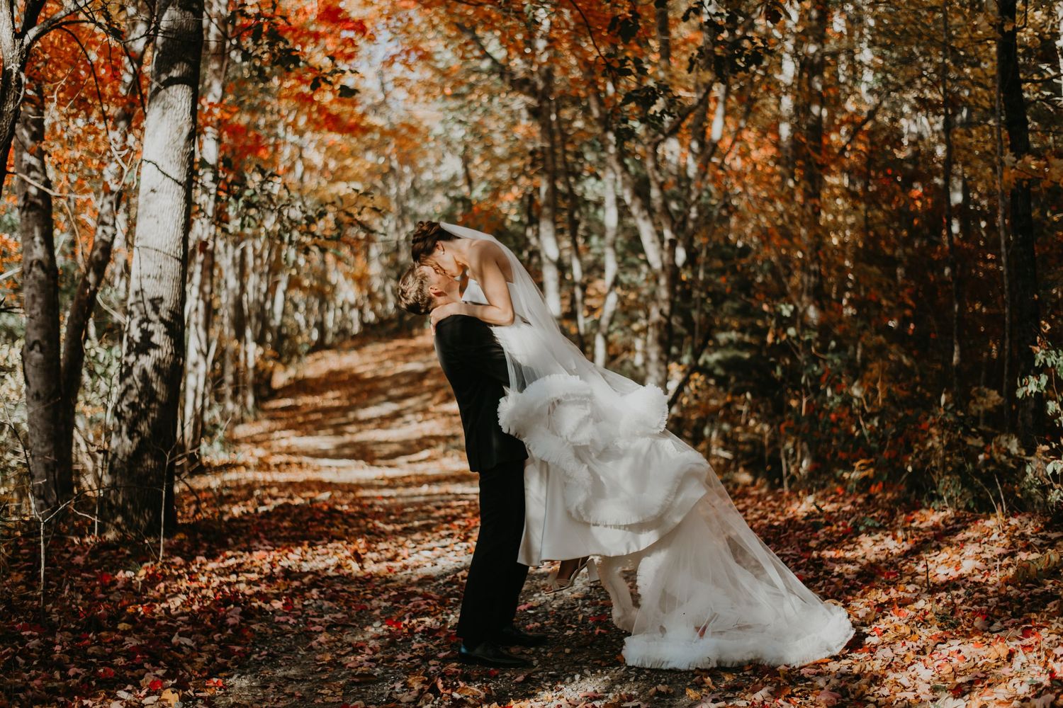A romantic wedding pose amongst autumn trees with flowing white dress and fallen leaves in North Carolina.
