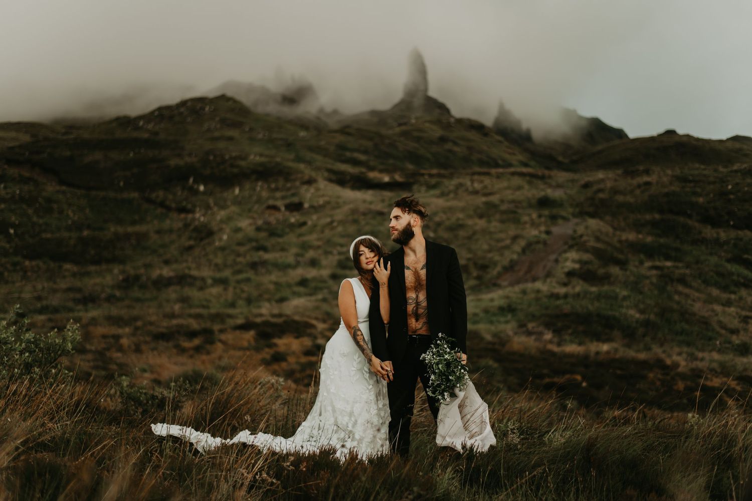 Wedding couple standing on misty mountainside in romantic pose with dramatic landscape.