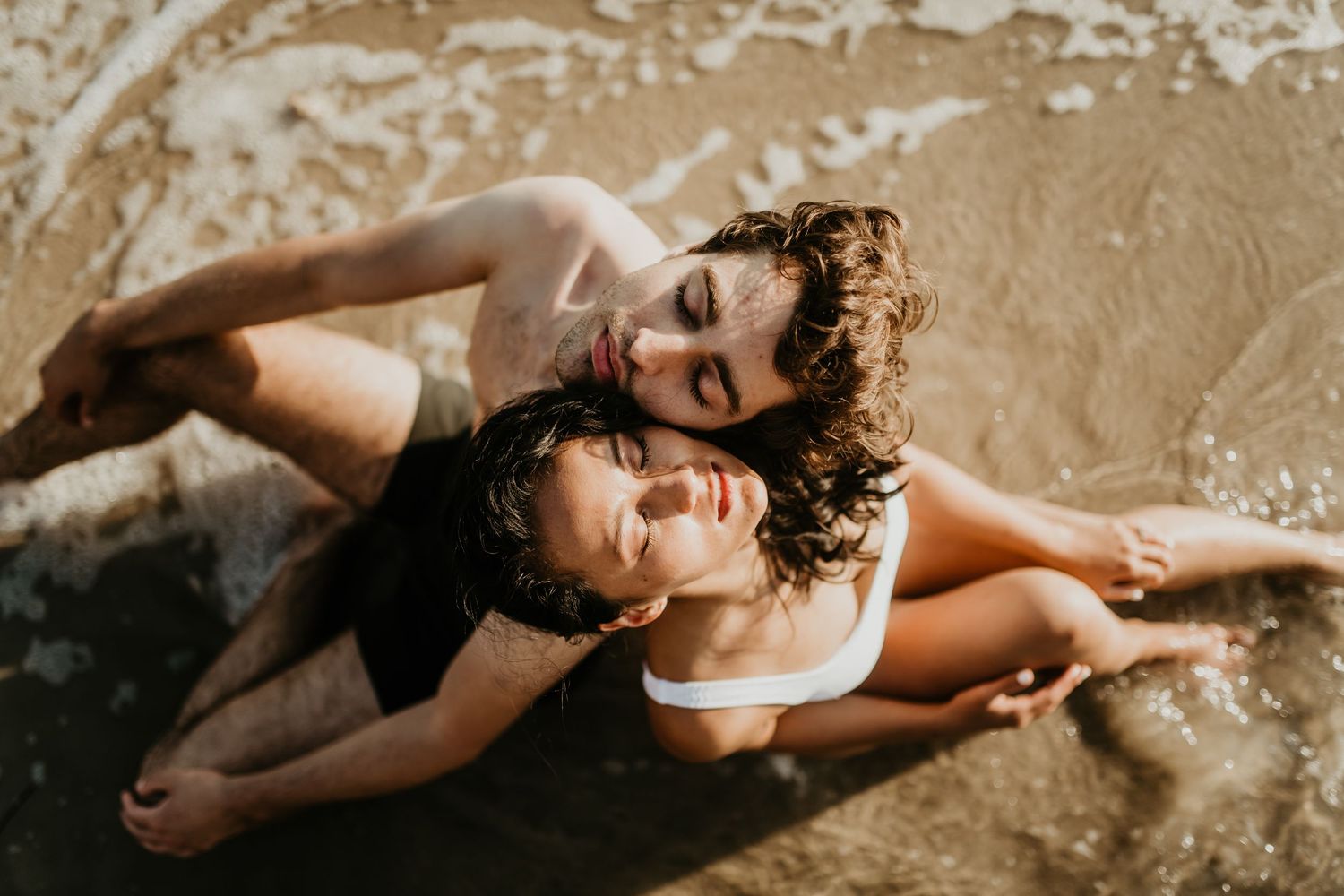 A person lays back in cream-colored water creating artistic ripples and movement in a sensual boudoir photoshoot.