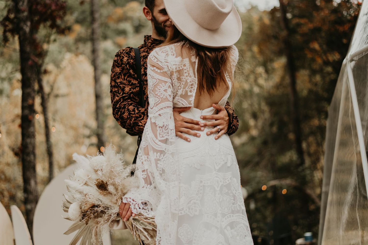 Intimate wedding couple poses under a clear umbrella surrounded by fall foliage and dried palm leaves.