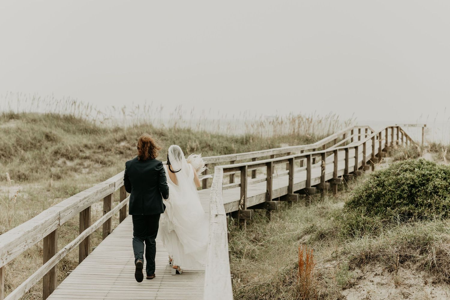 A couple walks hand in hand down a wooden boardwalk by the beach in south Carolina.
