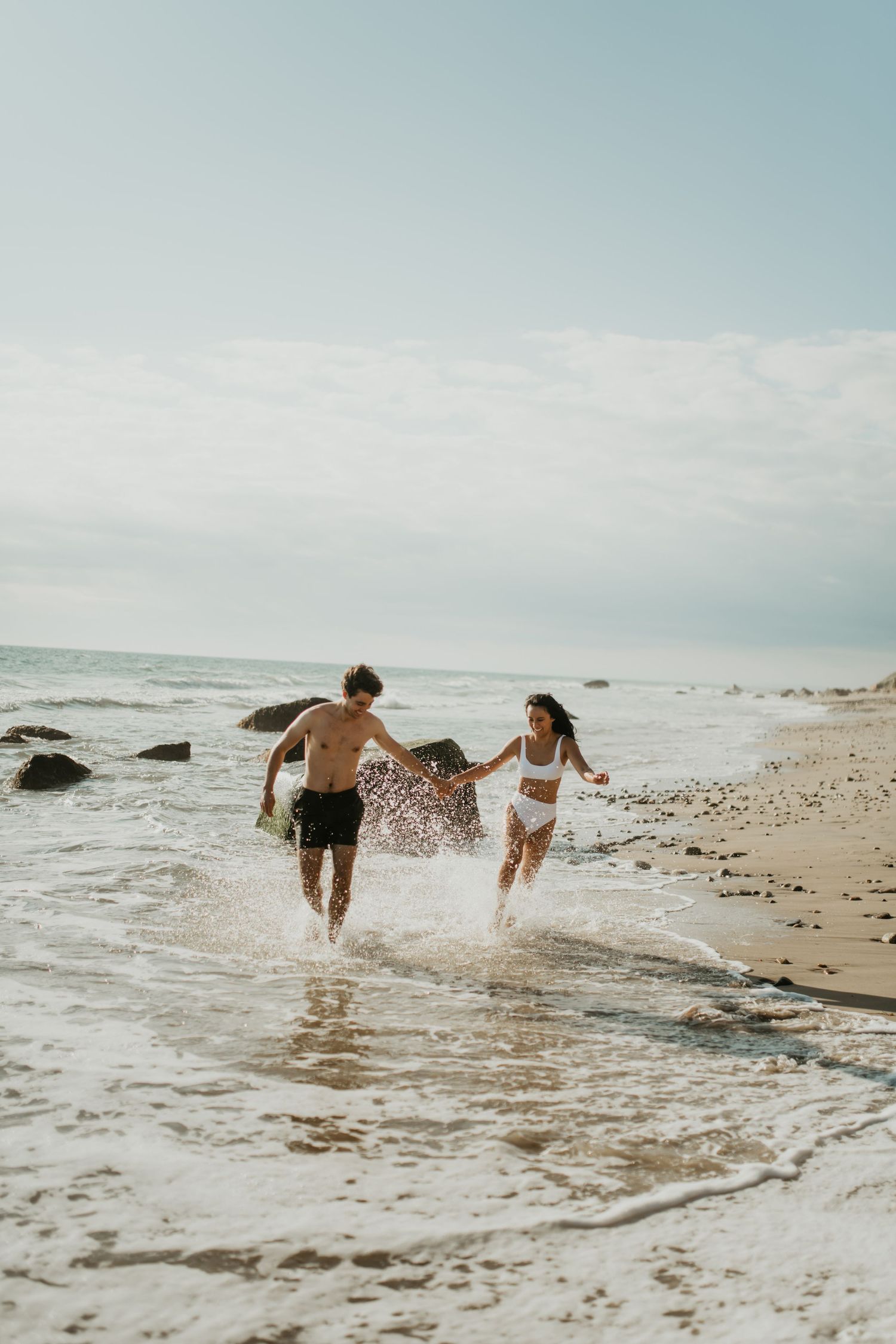 Two people splashing and running through ocean waves at the beach shore on a cloudy day.