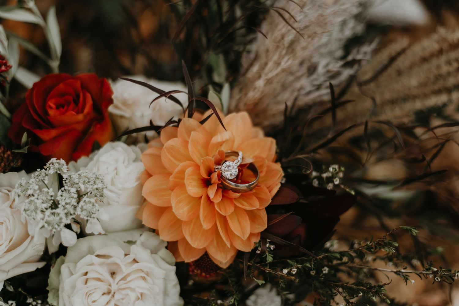Close-up of wedding floral arrangement with peach dahlia, red rose, and pampas grass.