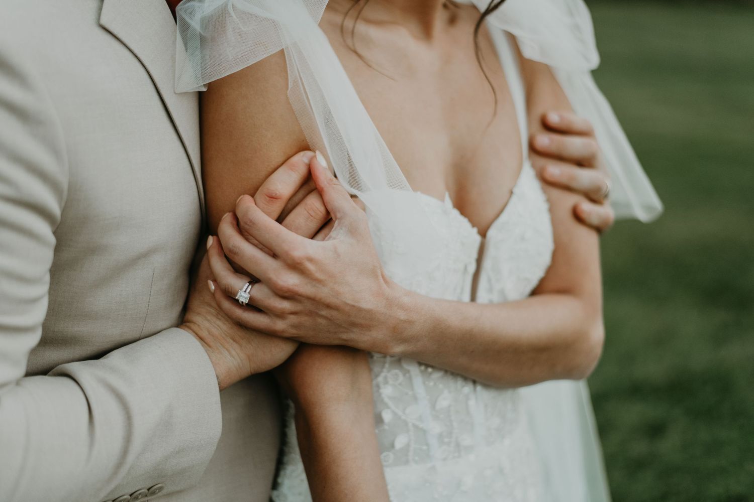 Close-up of embrace showing delicate lace wedding dress details and gentle hands.
