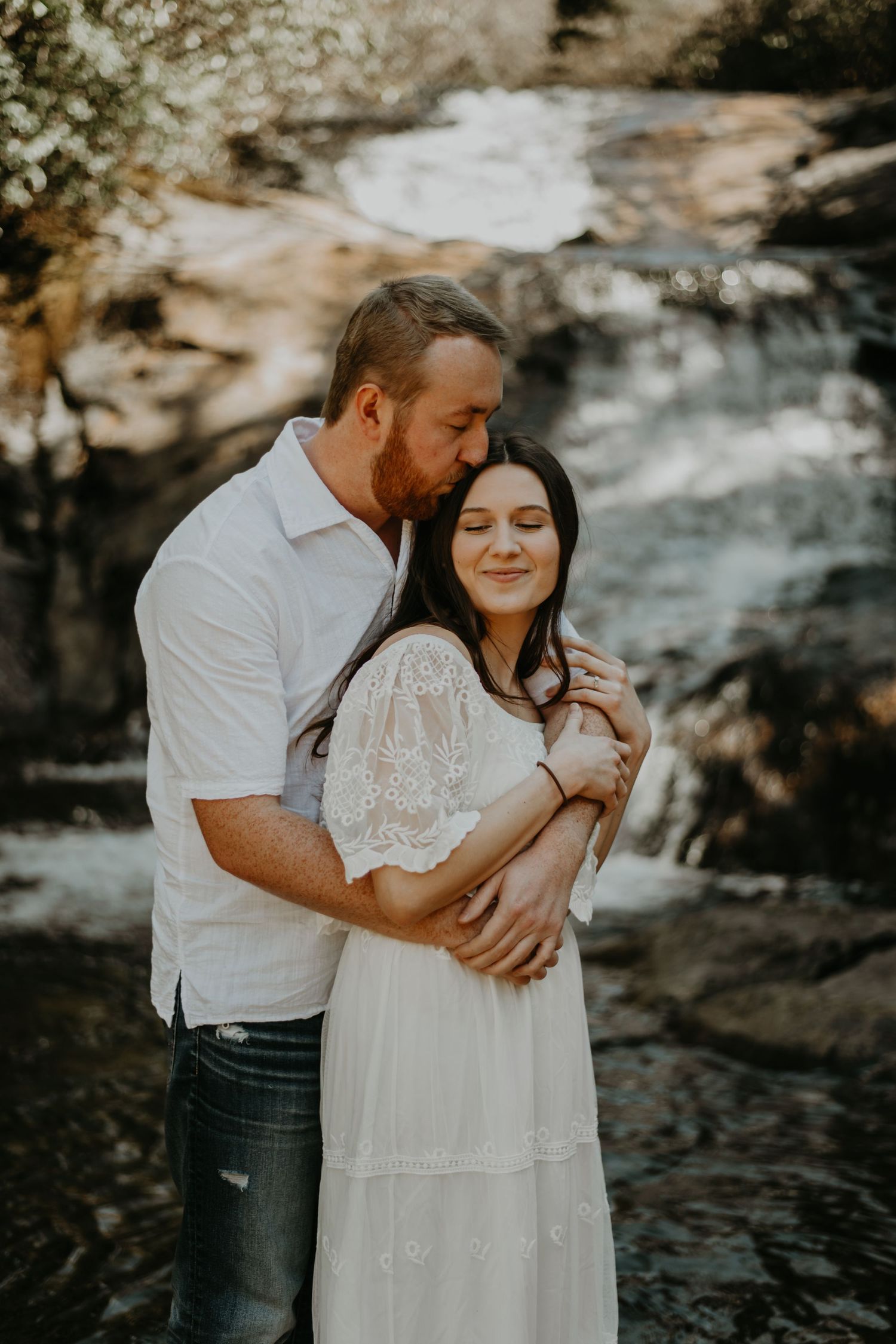 Intimate couples photoshoot by rocky stream with white lace dress in warm sunset light.