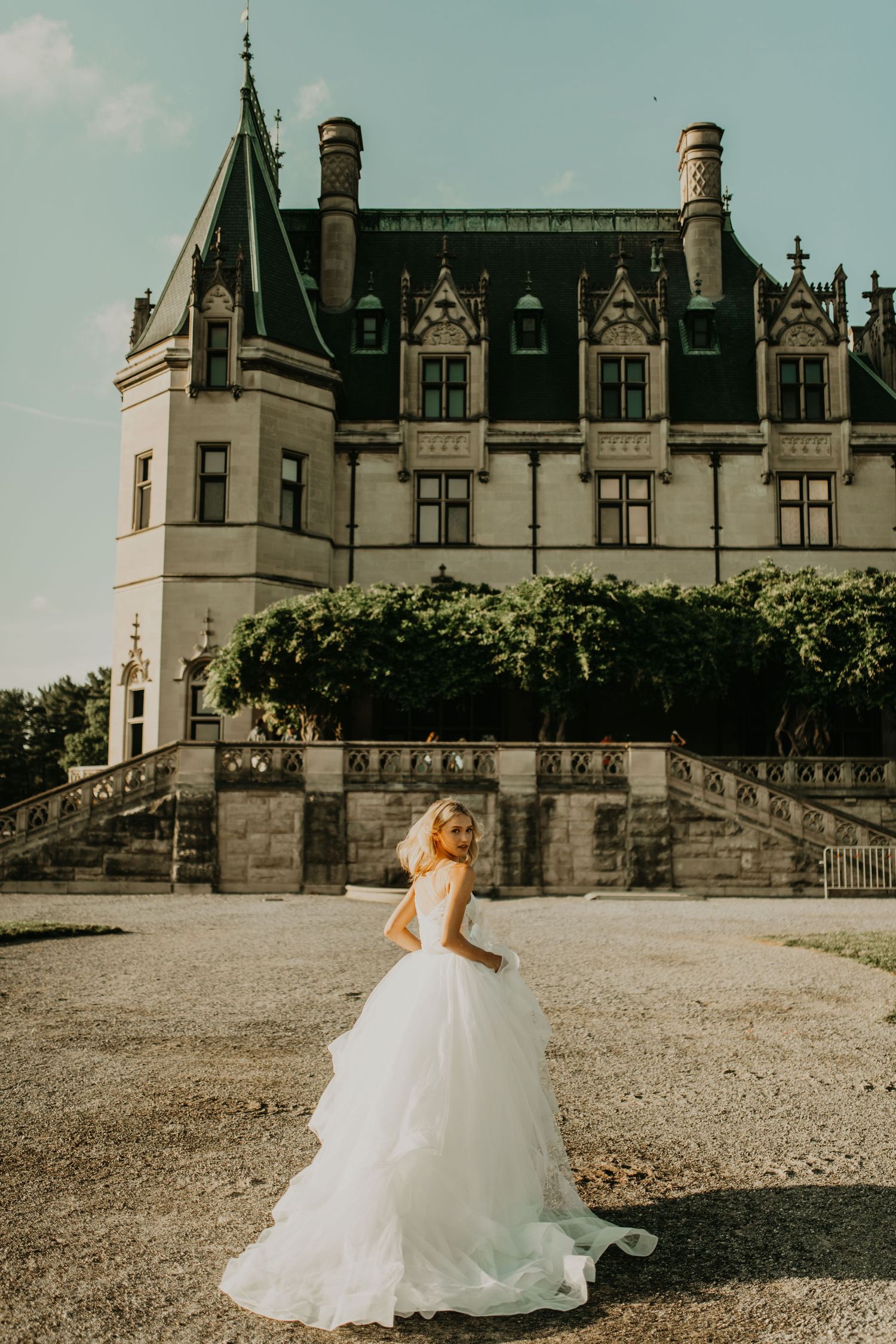 A bride in a flowing white gown poses in front of a majestic historic mansion in Asheville North Carolina.