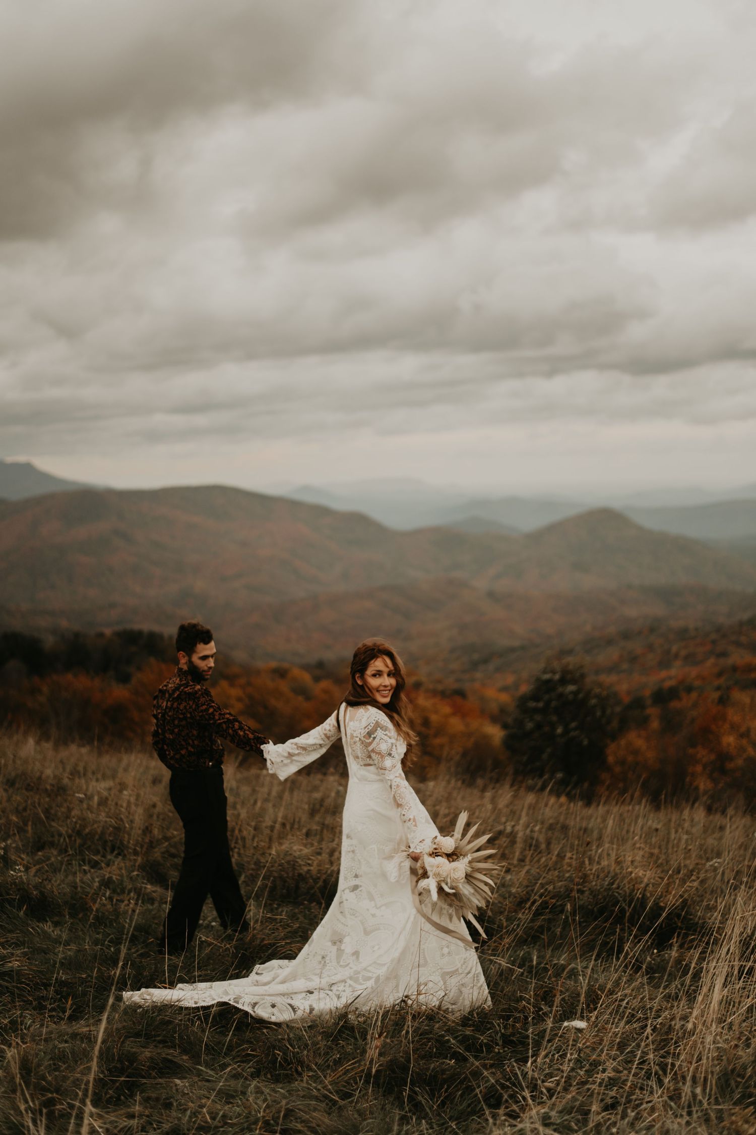 A couple dances together on a mountain ridge surrounded by autumn foliage and cloudy skies in North Carolina.