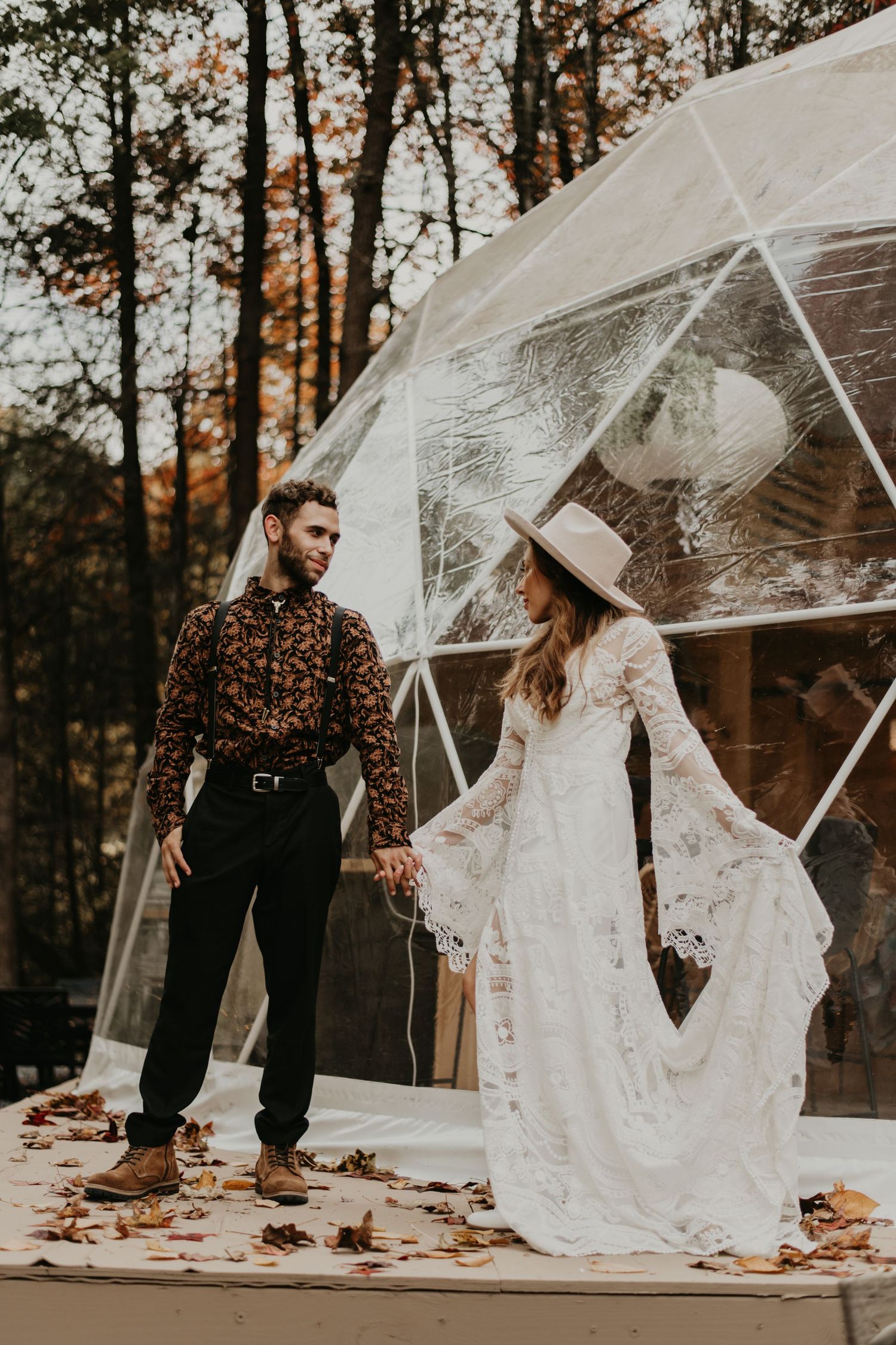 Wedding couple shares tender moment under transparent umbrellas on wooden platform surrounded by autumn leaves.