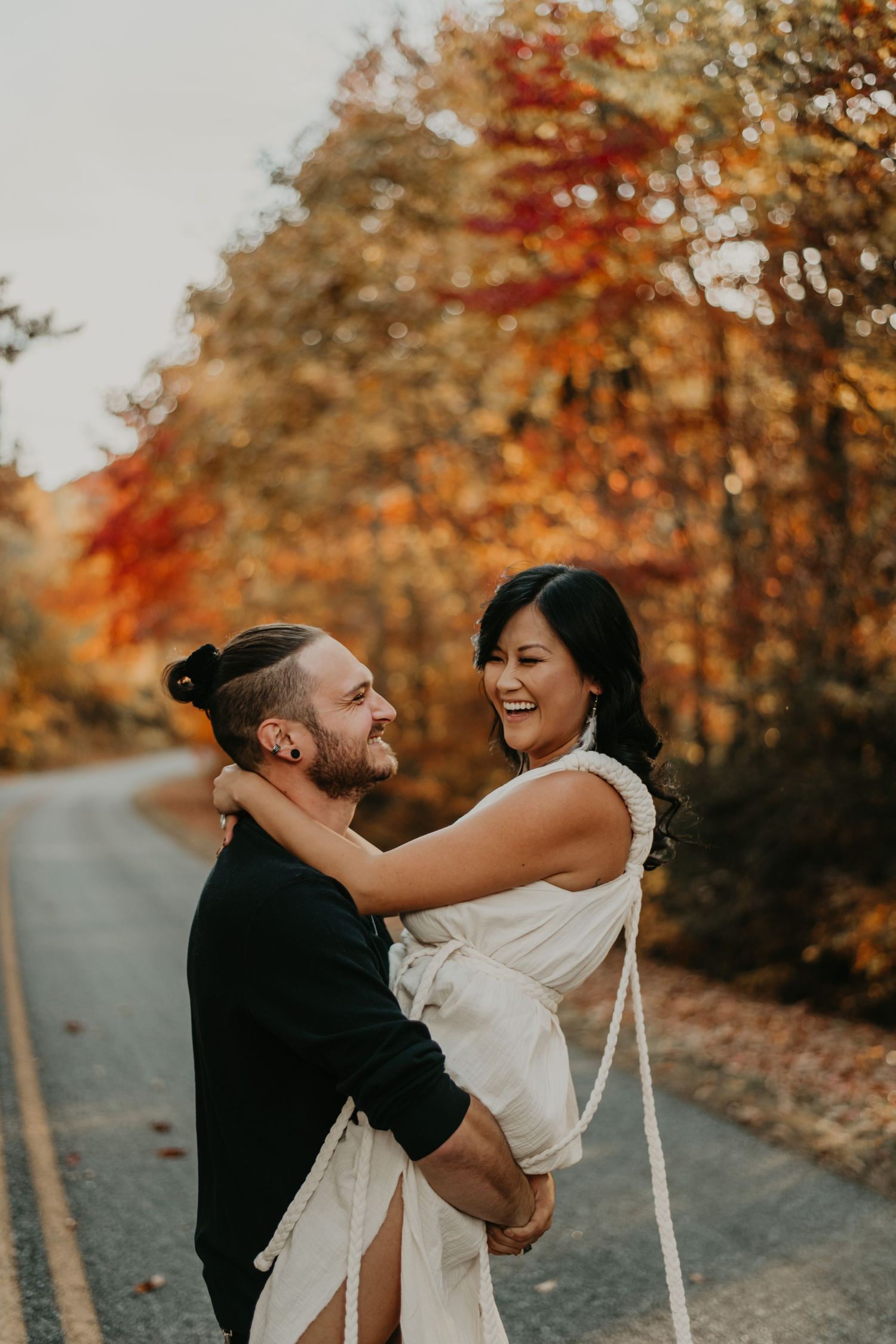 A joyful couple embraces and laughs together on a tree-lined path during autumn at sunset.