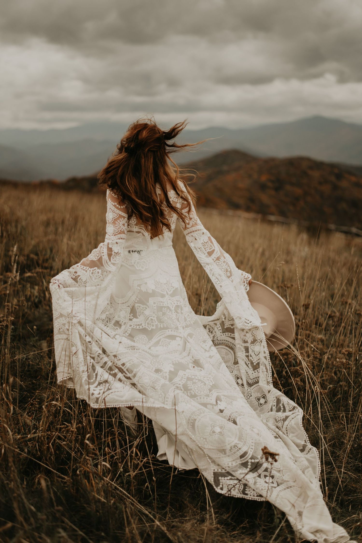 White lace veil flowing in the wind against a moody mountain landscape during golden hour.