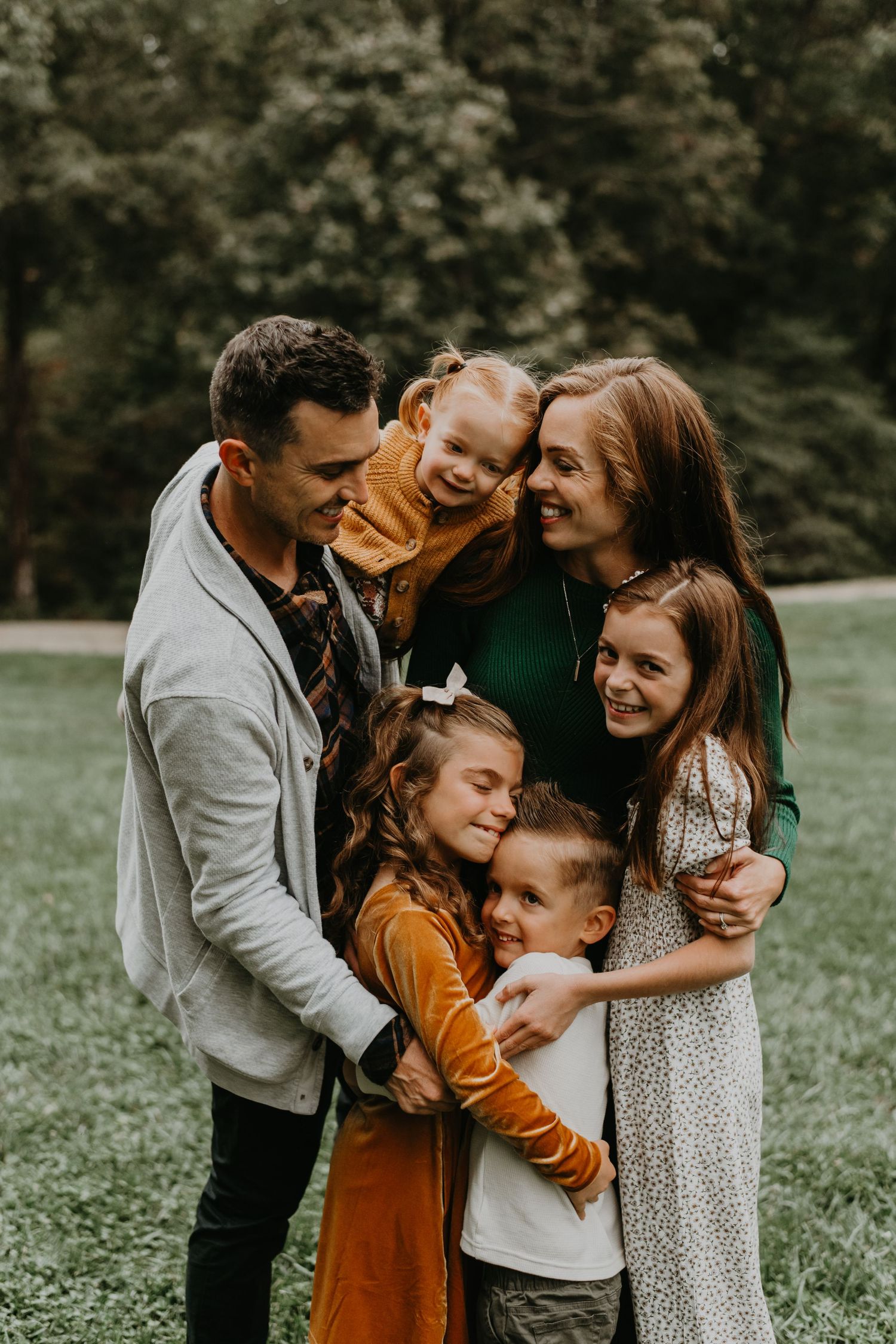 Family sharing affectionate moments together in a park setting with warm autumn colors and natural lighting.