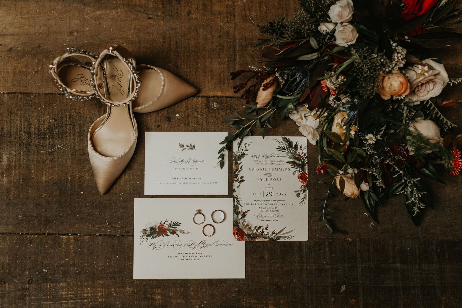 Wedding stationery and beige heels arranged with floral decorations on wooden background.