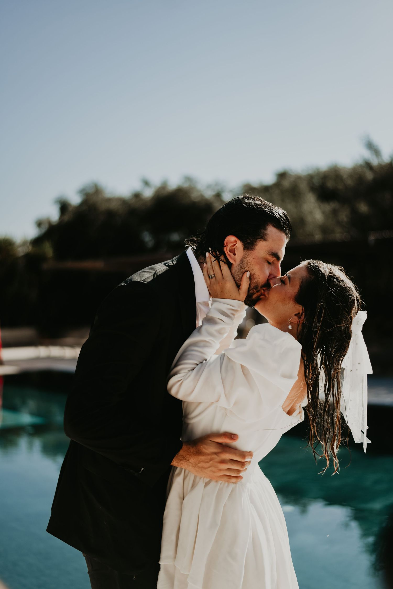 A romantic wedding kiss captured at poolside with sun-drenched lighting in Italy.