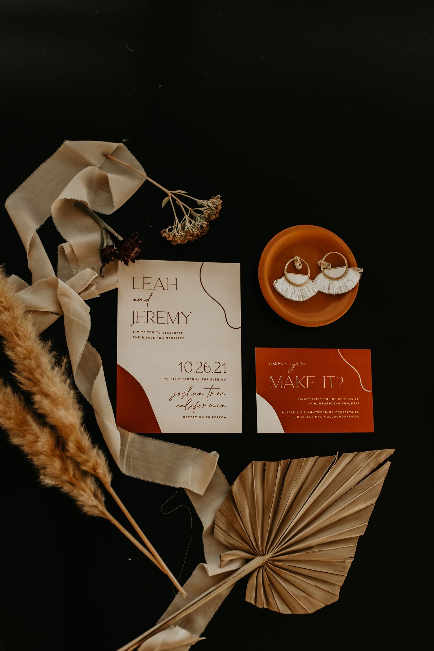 Modern wedding invitation suite with terracotta and neutral tones featuring dried flowers and paper details.