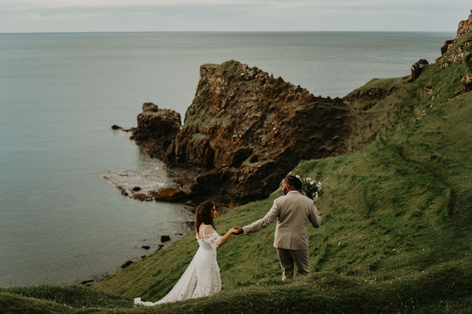 Couple holding hands on dramatic coastal cliff overlooking ocean in isle of Skye Scotland.
