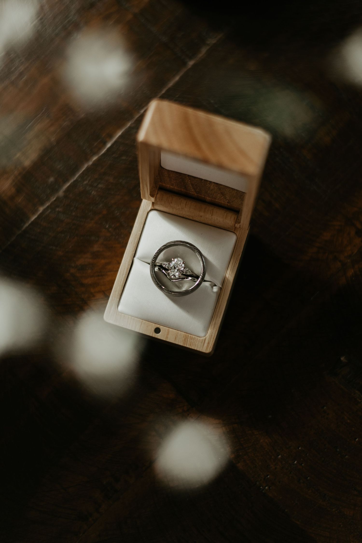 Diamond engagement ring in wooden box with moody lighting and bokeh effects.
