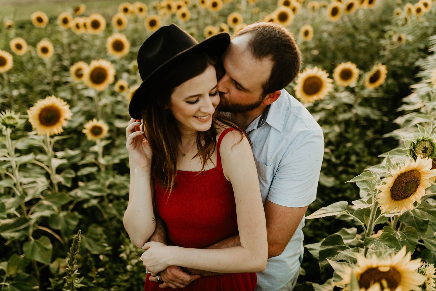 A romantic couple shares tender moments in a vibrant sunflower field during golden hour.