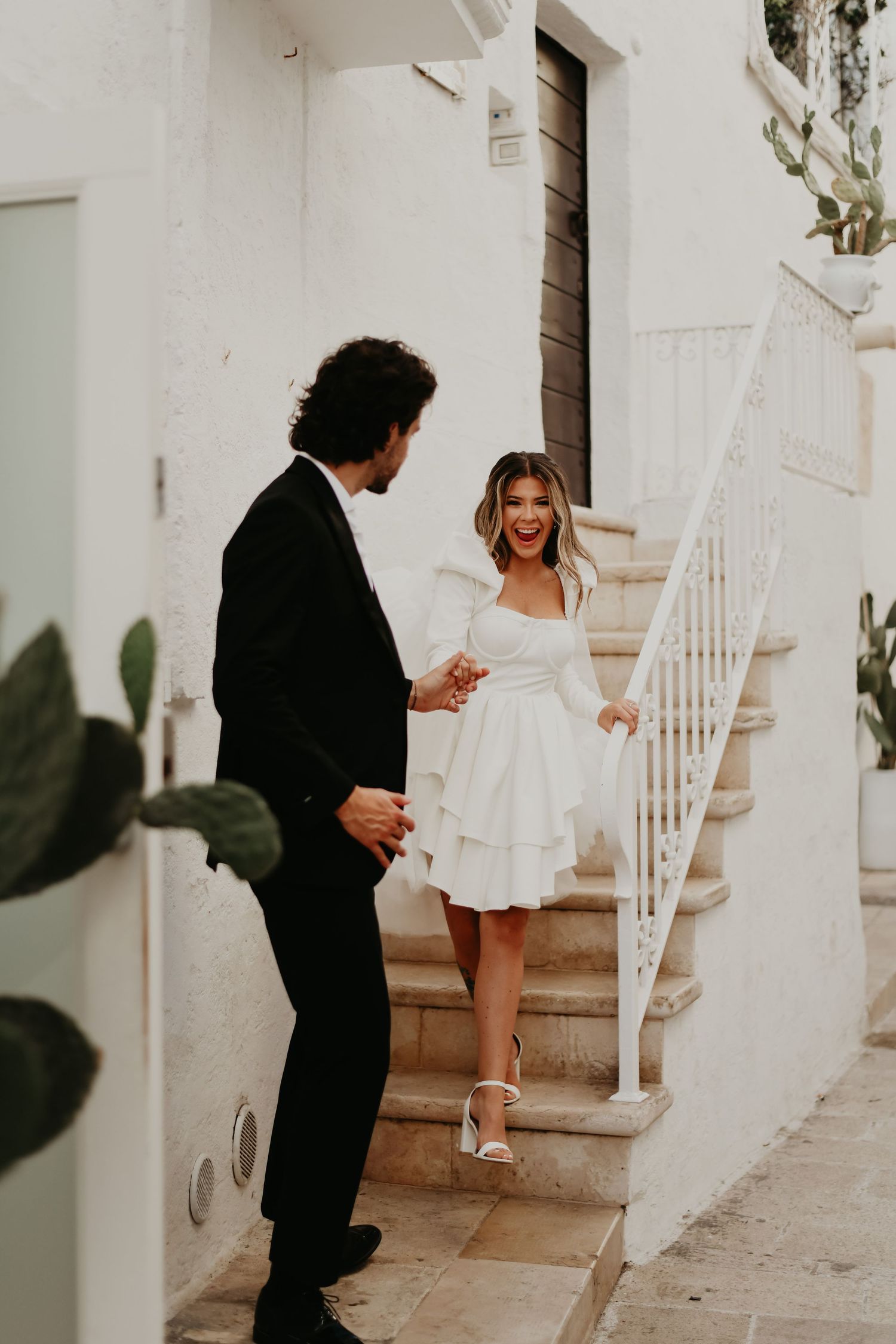 A couple shares a joyful moment on white stone steps of a Mediterranean-style building in Monopoli Italy.