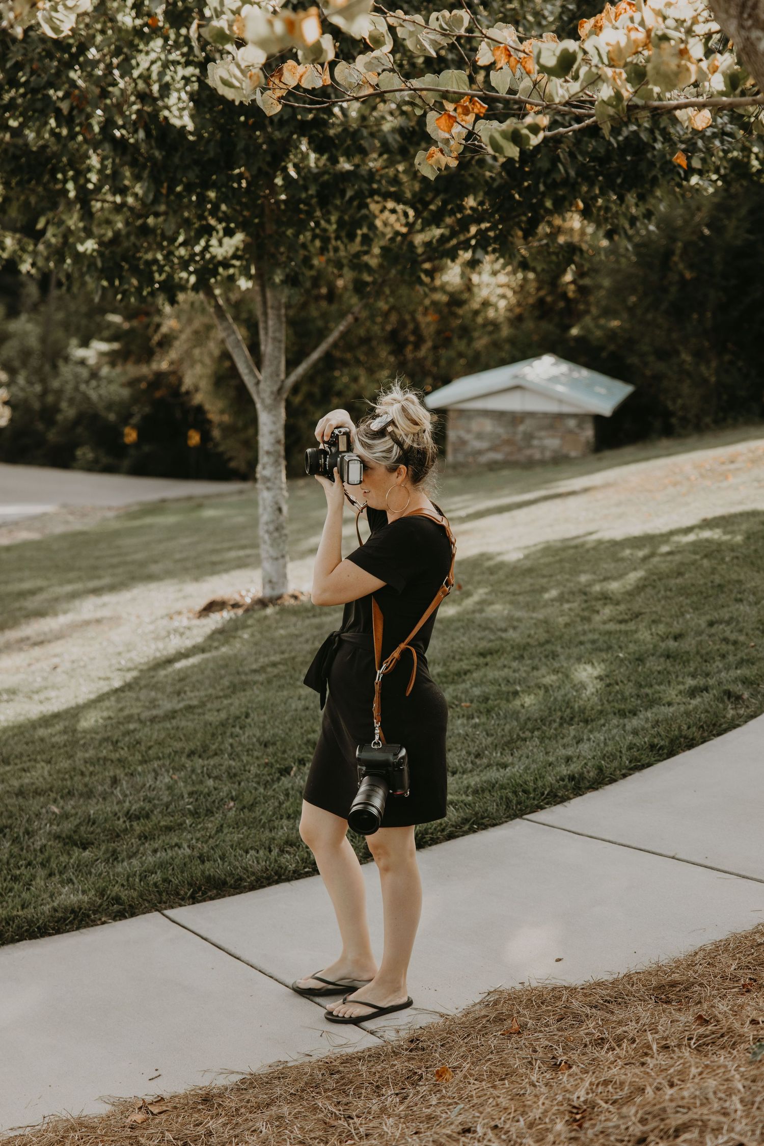 A photographer in black captures images outdoors during golden hour with trees and lighting in background.