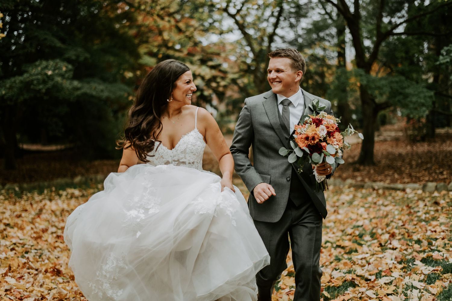 Wedding couple dances playfully through fallen autumn leaves in a woodland setting in North Carolina.