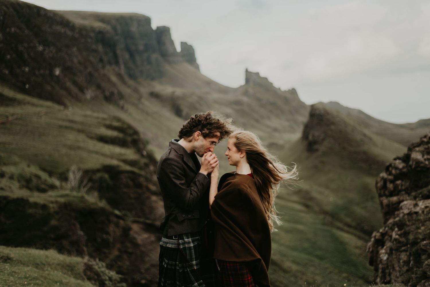 A couple embraces on a misty cliff overlooking dramatic Scottish Highland mountains in isle of Skye Scotland.