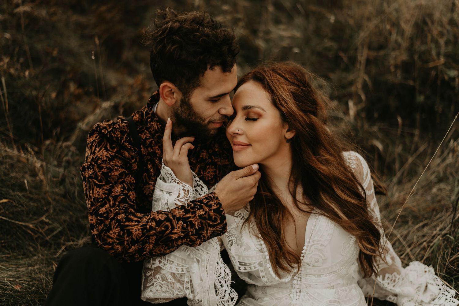 An intimate moment between a couple in wedding attire on a mountaintop during sunset.