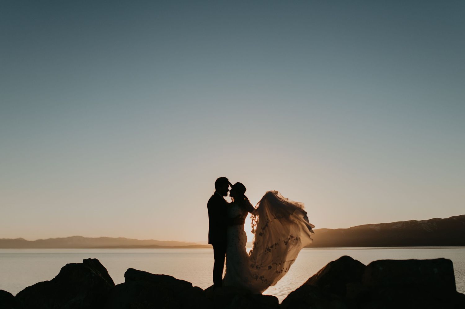 Silhouetted couple embracing during sunset near a mountainous waterfront landscape in Utah.