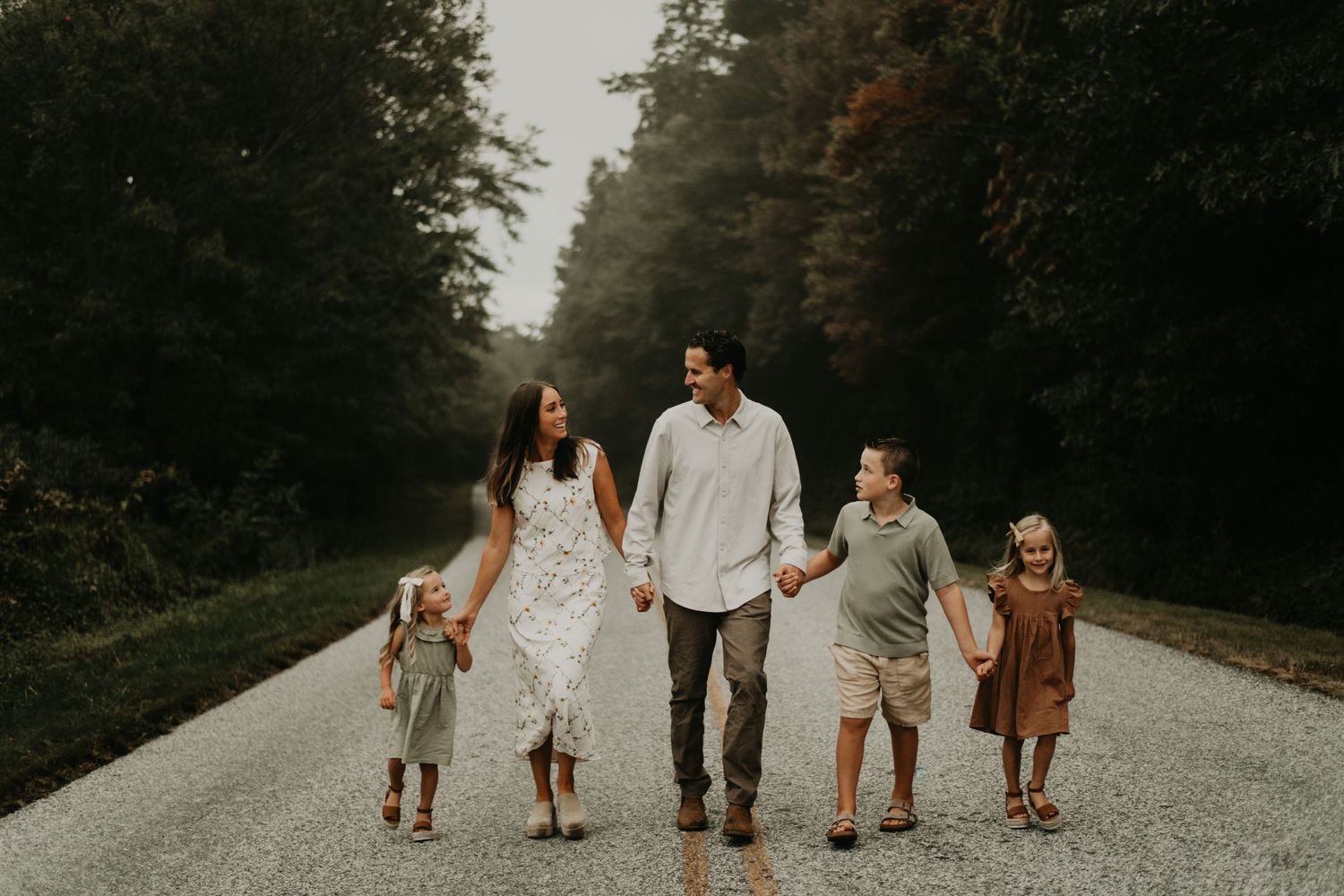 Family walking hand in hand down tree-lined gravel road at dusk in Asheville North Carolina