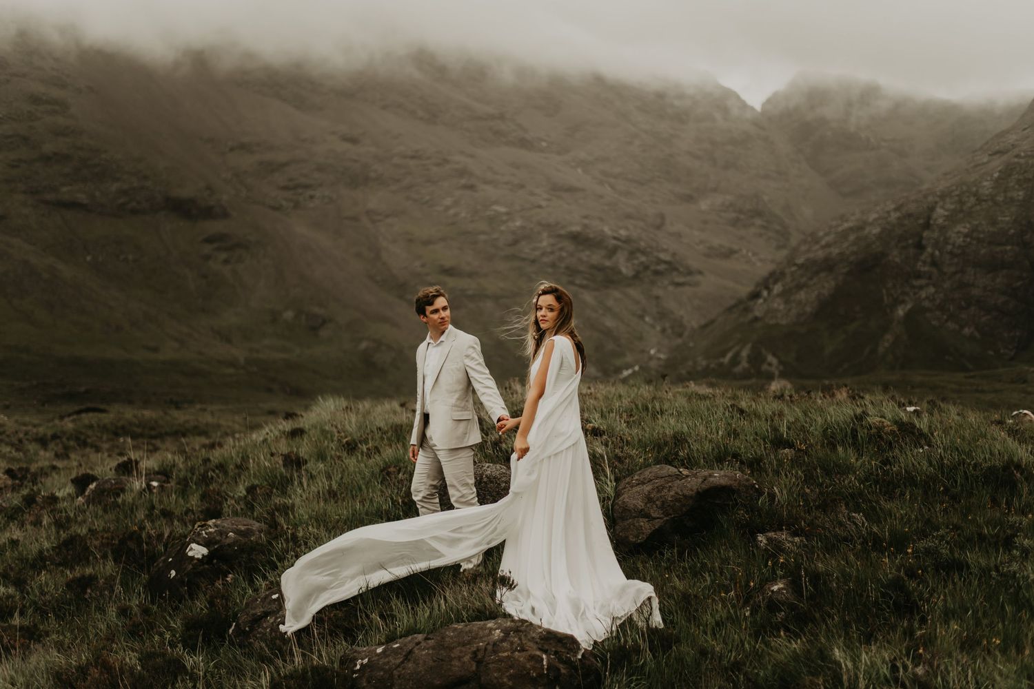 Wedding couple walking along dramatic mountain ridge in flowing dress in Isle of Skye Scotland.