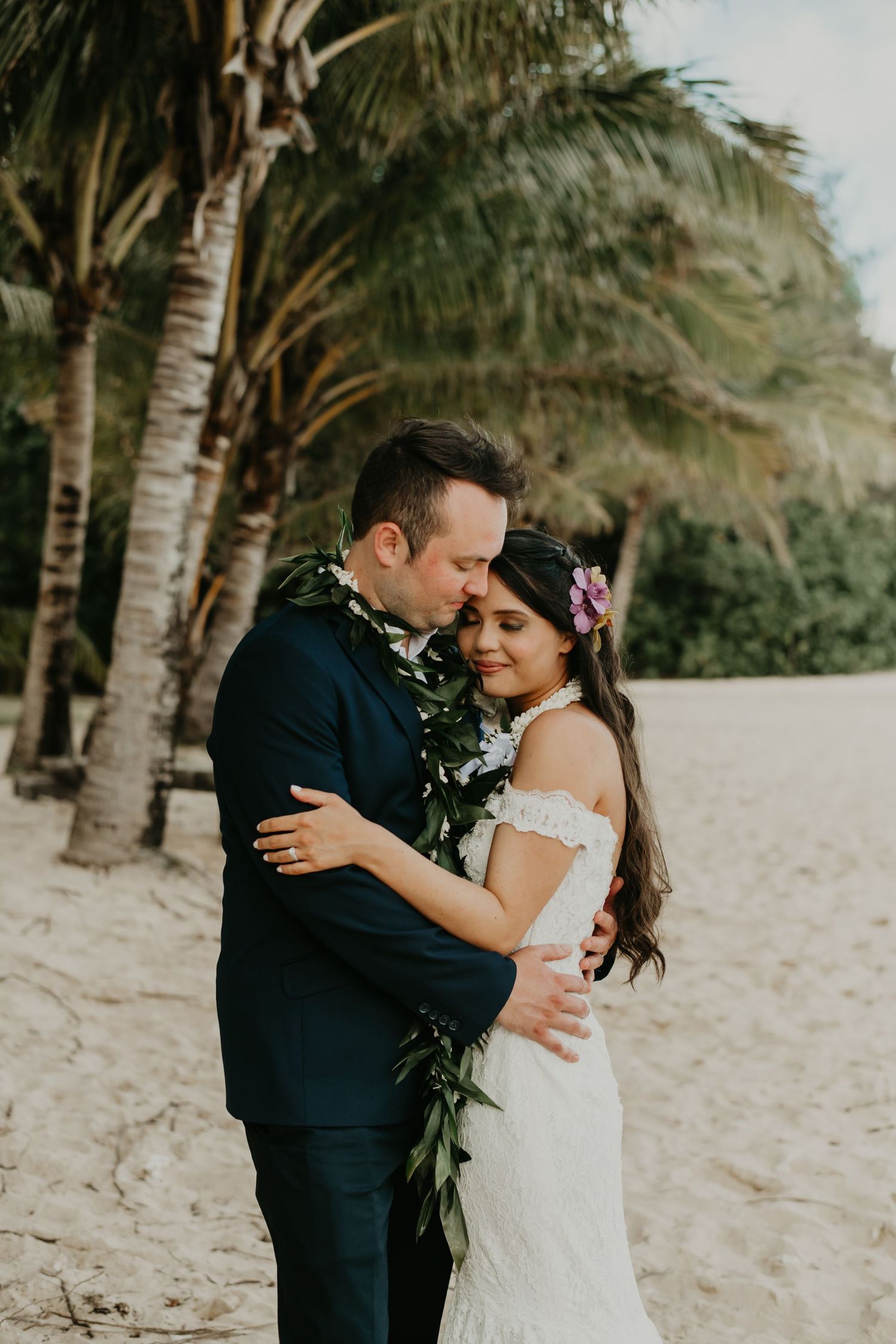 A couple embraces on a tropical beach with palm trees in the background in Hawaii.