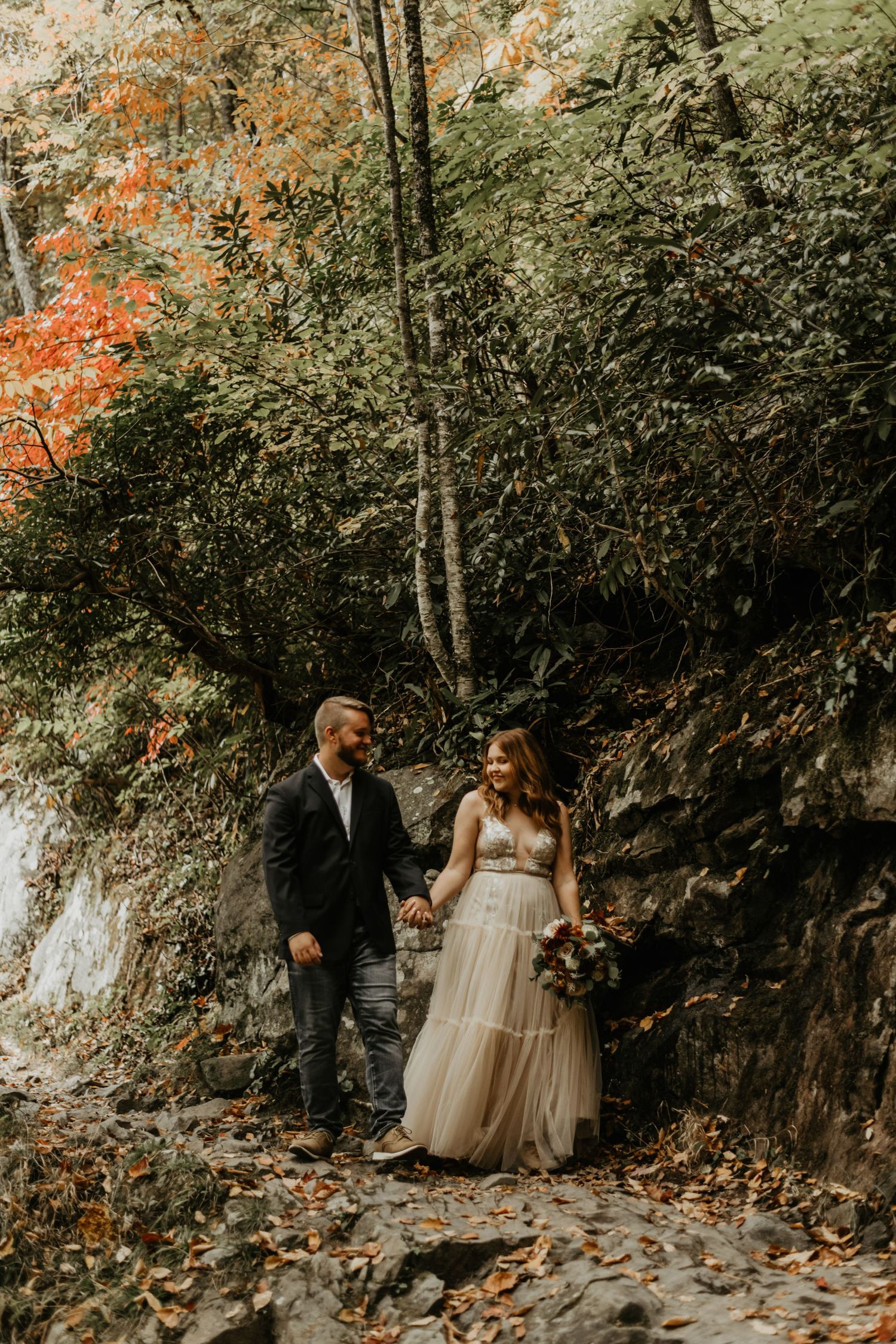 Romantic autumn woodland wedding portrait with couple walking along rocky path.