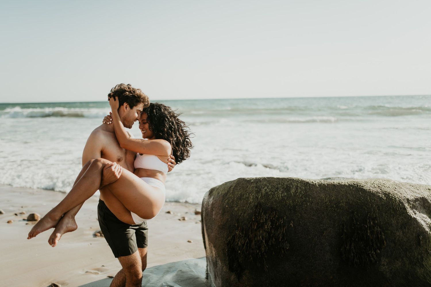 A romantic couple embraces during their beach engagement photoshoot as waves crash behind them.