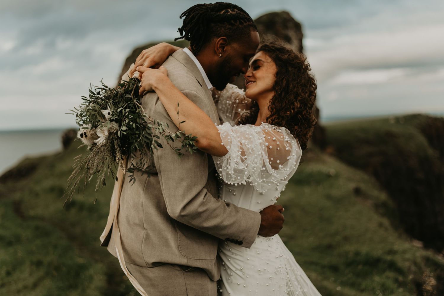 A romantic wedding couple embraces on a scenic clifftop at sunset with moody skies in Isle of skye Scotland.