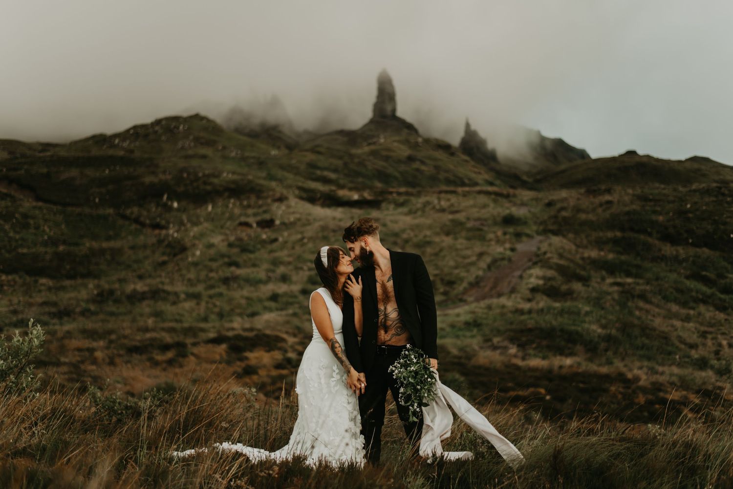 A couple shares an intimate moment against a misty Scottish mountain backdrop in isle of Skye Scotland.