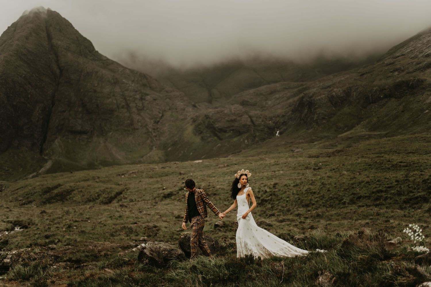 A dramatic wedding photo with couple standing against misty mountain landscape.