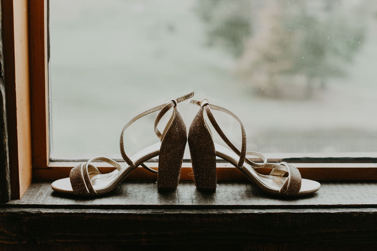 Brown strappy wedding heels displayed on windowsill with soft lighting.