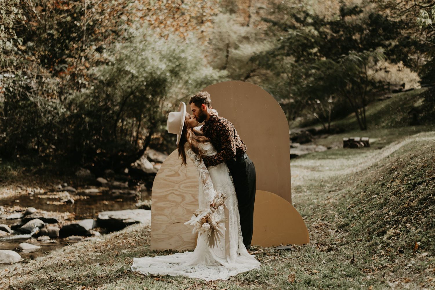 Artistic wedding photography with copper arch framing couple against mountain landscape.