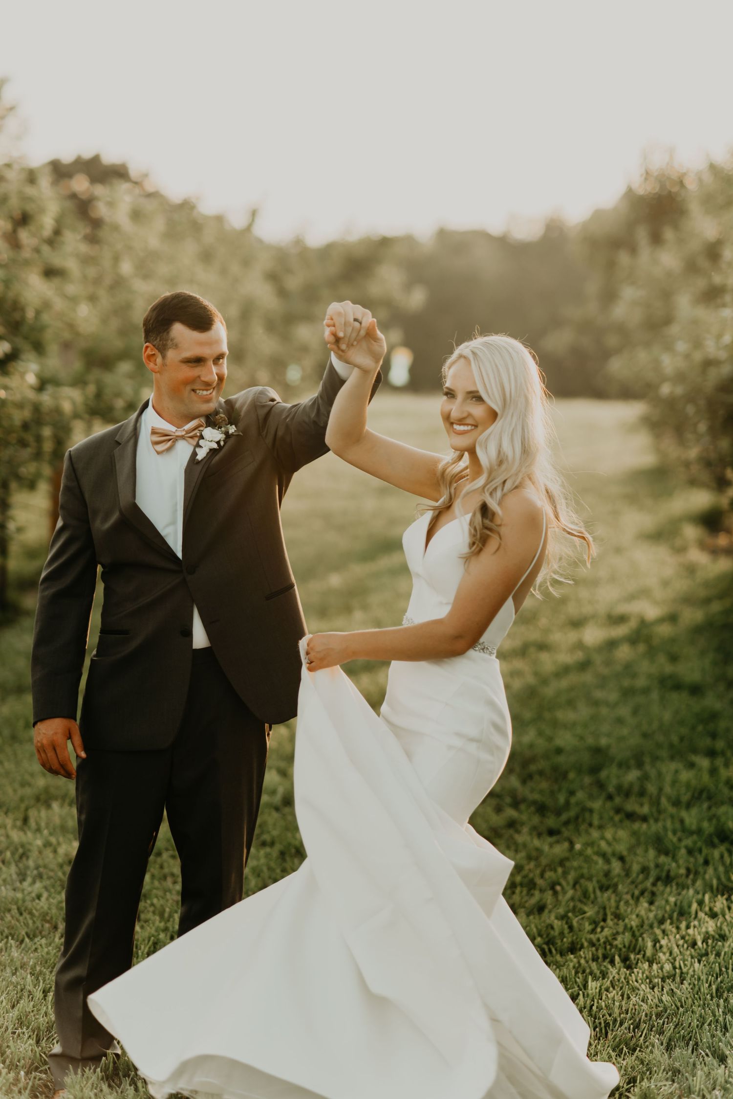 A joyful wedding dance moment captured in golden sunlight on a grassy hillside in North Carolina.