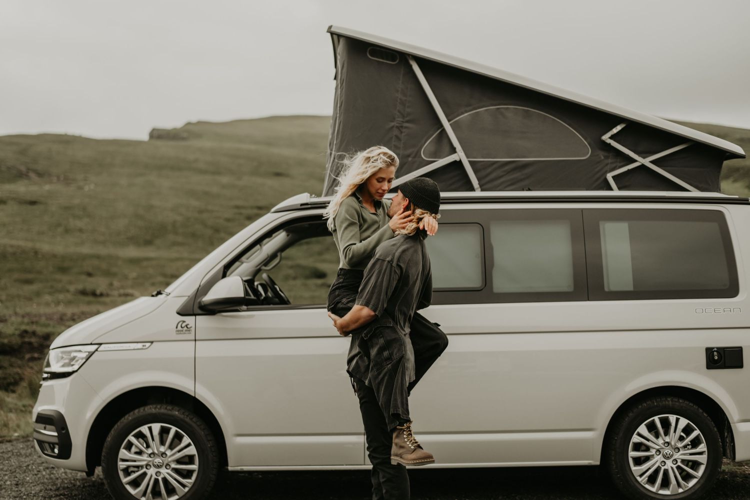 Camper van with pop-up roof parked in misty hills while someone stands by the open door.